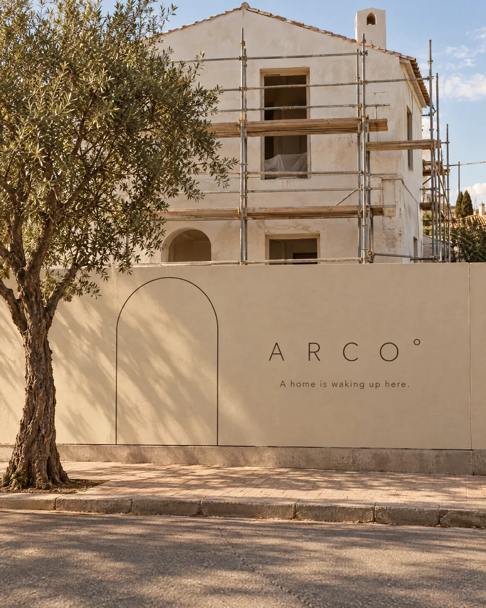 גדר אתר שיפוץ ממותגת ARCO° עם ציור קשת, מול בית בשיפוץ ועץ זית